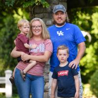 The Brinegars pose together as a family and smile for the camera. Jennifer and Michael are standing side by side, Bennett is standing in front of Michael, and Jennifer is holding Jeremiah on her hip.