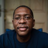 A close-up portrait of Jerome, smiling slightly, in front of the door to his home.