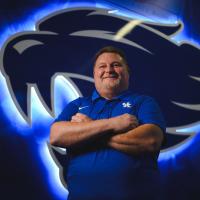 Jimmy stands and smiles in front of a large glowing wildcat logo.