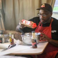 A candid photo of Joshua inside of a camper adding spices into a mixing bowl.