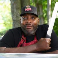 A photo of Joshua posing for the camera with a long metal slicing knife in his hand.