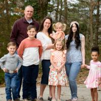 Julie and her entire family stand smiling together with Jennifer and her daughter in an outside setting.