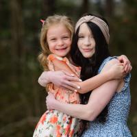 Julie and Jennifer, a young woman with dark brown hair, embrace and smile with one another.