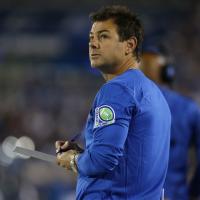 Frank Buffano, a middle-aged white man with brown hair, looks up and over his shoulder during a football game. He holds a clipboard and a pen and is wearing a blue UK coaching shirt.