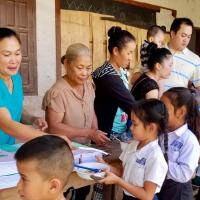 Khay regularly returns to Laos to serve the communities there. He's helping hand out supplies to young school children.