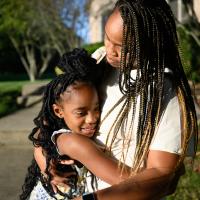 A close-up photo of Kristen’s mother Krissalyn, an African-American woman with dark brown and blonde braids, hugging her. Krissalyn is wearing a long white dress.