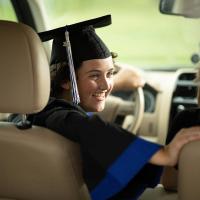 Kylee Tyson sitting in the driver's seat of a car, wearing her graduation cap and gown.