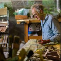 We see Lynn through the window to his studio, working on one of his frescoes.