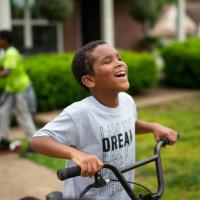 A candid photo of Malakai smiling while pushing his bike outside.