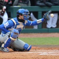 An action shot of Marshall catching a ball. He is kneeling on the baseball field behind a batter. His catcher’s uniform is covered in dust.