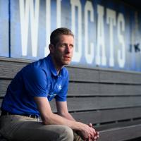 A candid photo of Matt sitting on the bench in the dugout and looking off into the distance.