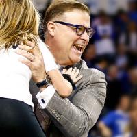 Coach Mitchell picks his daughter up for a hug while looking really happy at a basketball game.