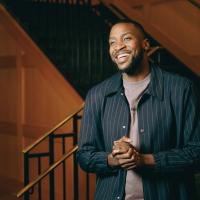 A photo of Michael clasping his hands together as he smiles and looks off camera.