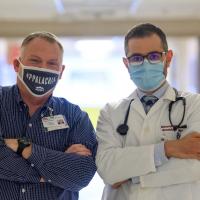 A portrait of Michael and Dr. Shanshal, posing with their arms crossed. Both are wearing masks.