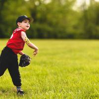 Max throws a baseball in his team uniform. His insulin pump is visible on the back of his upper arm.