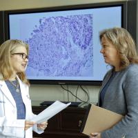 A candid photo of Dr. Kolesar and Dr. Miller having a conversation in front of a TV with an image of cells on it.