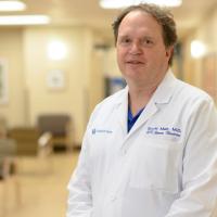 Dr. Scott Mair, an older white man with brown hair, poses for the camera in front of a sports medicine exam room.