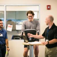 Peter's physical therapists talk while he rides a stationary bike.