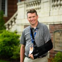 Leonard wears a black sling to support his arm and shoulder, but still smiles.