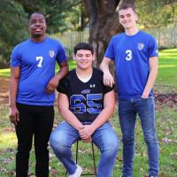 In an outside setting, Remilson stands next to his brother Alex who is seated and beside Alex is his brother Zach.