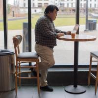 Roger stands at a tall cafe table to work on his laptop.