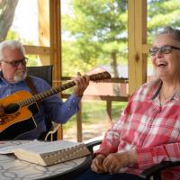 A candid photo of Ronnie and Becky on their porch. Ronnie is playing the guitar while Becky smiles.