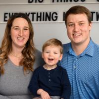 Rory is seated on the couch in between his parents as they all smile widely at the camera.