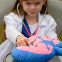 Taytum holds her toy stethoscope to a plush heart. She is in the background of the photo and is blurred out. The heart is in focus.