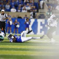 Terry is lying on the field after being tackled while still holding the ball—moments after he suffered his injury. His left leg is bent while his right leg remains straight. Opposing players and a referee can be seen in the background next to him.