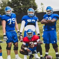 A posed photo of Terry and five of his teammates, all dressed in practice gear, with his teammates surrounding him as he squats in front of the group.