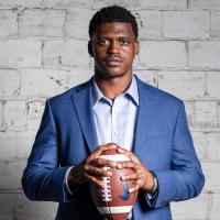 A portrait of Terry, dressed in a blue blazer and light blue button-up shirt, holding a football and looking directly at the camera.