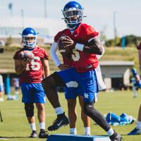 An action shot of Terry holding a football at practice and running drills, dressed in a red jersey over his practice uniform.