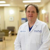 Dr. Mair stands in a hospital hallway with his arms by his side as he looks into the camera.