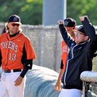 Trent looks to his teammate and gives him a half smile. They are standing on a baseball field in their Tigers baseball uniform and caps.