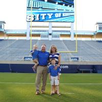 Coach Stoops stands with his wife and sons in front of the goal at Kroger Field. They are all wearing blue.