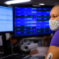 An over-the-shoulder shot of Whitley wearing a face mask and looking at a computer screen.