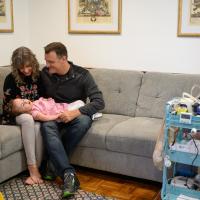 Karla and Gavin Duerson sit on the couch with Wylie sitting in their laps. Gavin is a white man with short brown hair, and he is wearing a gray pullover, blue jeans, and sneakers.