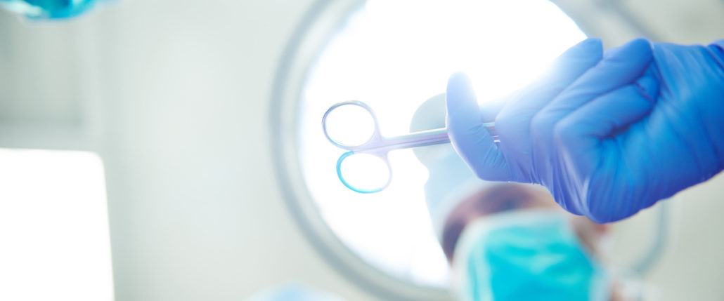 A surgeon in an operating room holds scissors.