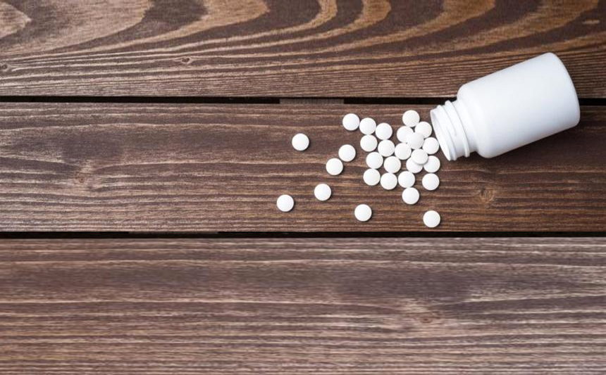 A bottle of white tablets are spilled on a wooden table.