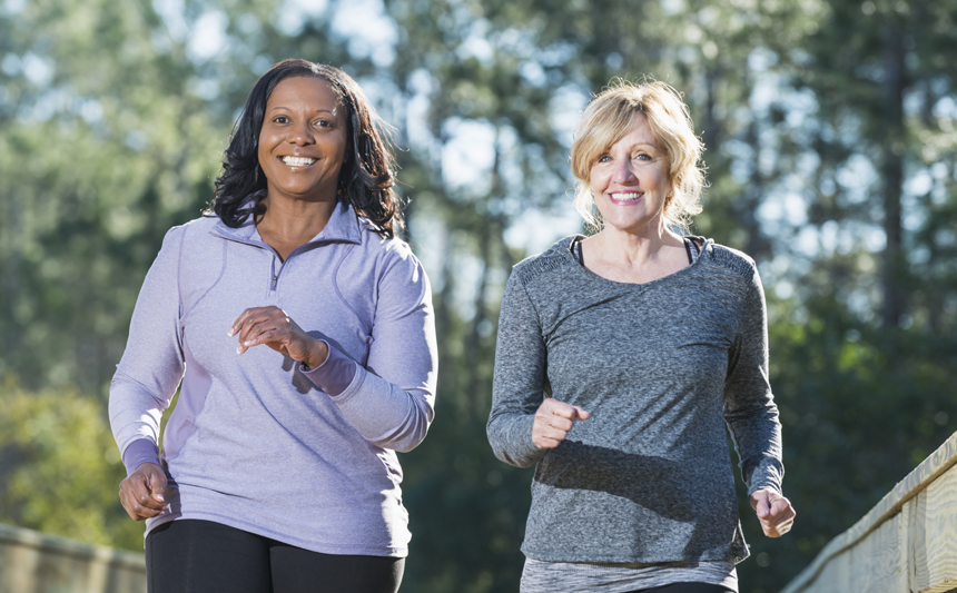 Two middle-aged women walking briskly in the park.