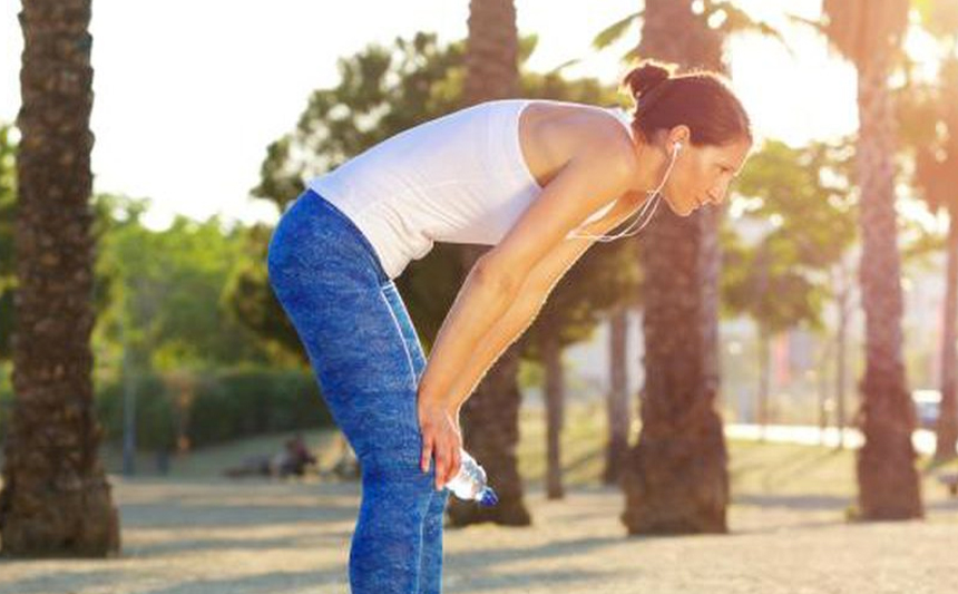 A woman pauses from exercising, resting her hands on her thighs.