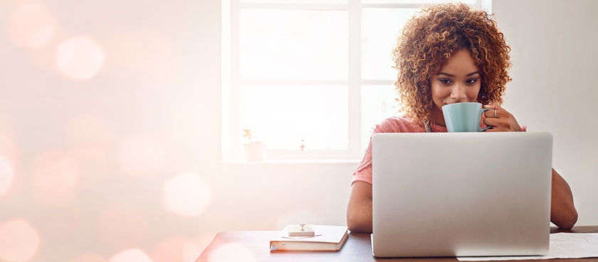 A woman drinks coffee while working at her laptop.