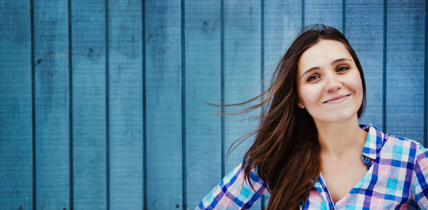 A dark-haired woman stands in front of a blue barn and smiles.