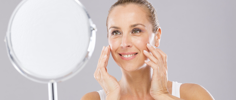 A woman touches her face as she looks into the mirror.