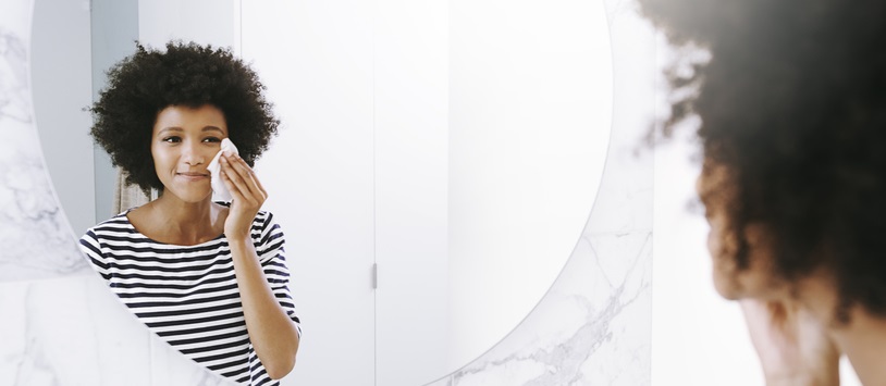 Young woman washes her face while looking in mirror.